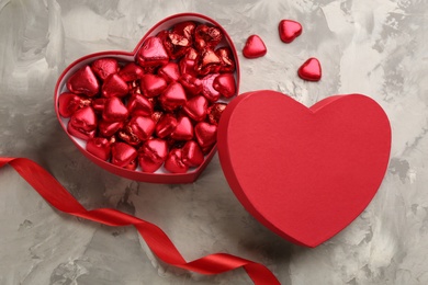 Box of heart shaped chocolate candies and ribbon on light grey table, flat lay