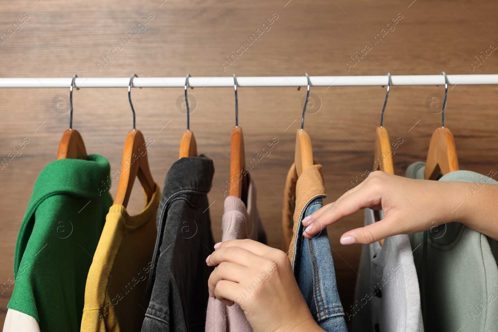 Photo of Woman choosing clothing with hangers near wooden wall, closeup