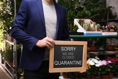 Business owner holding sign with text SORRY WE ARE CLOSED QUARANTINE in flower shop, closeup