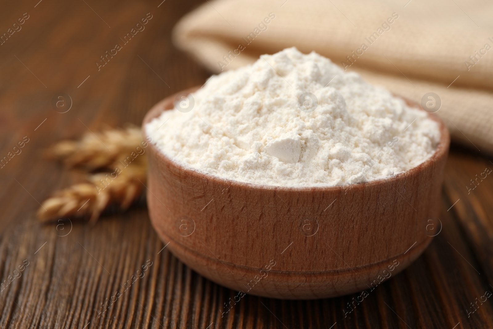 Photo of Bowl of organic wheat flour on wooden table, closeup