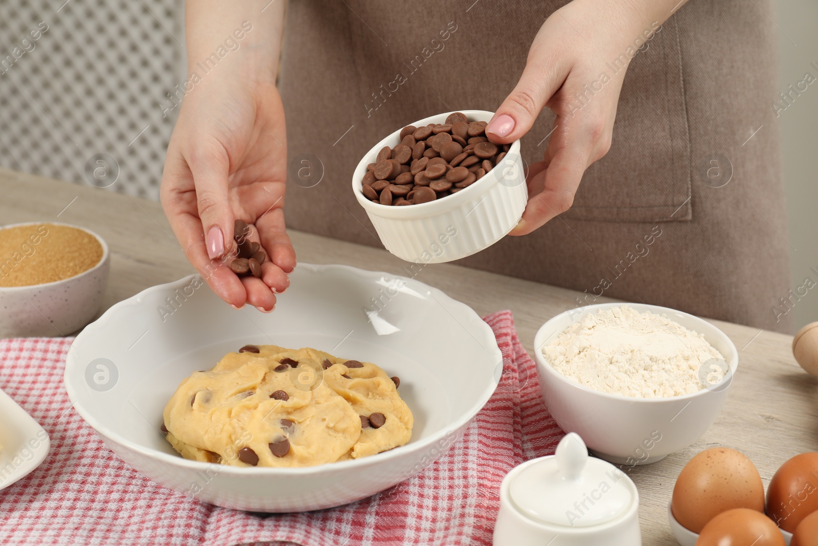 Photo of Cooking sweet cookies. Woman adding chocolate chips to dough at table in kitchen, closeup