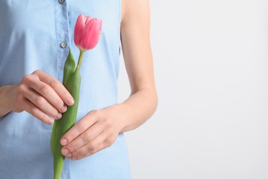 Girl holding beautiful spring tulip on light background, closeup. International Women's Day