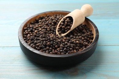 Photo of Aromatic spice. Black pepper in bowl and scoop on light blue wooden table