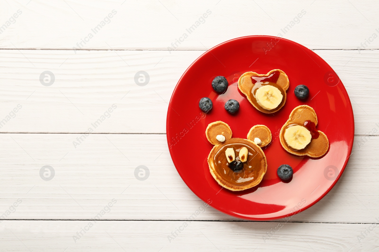 Photo of Creative serving for kids. Plate with cute bears made of pancakes, berries, banana and chocolate paste on white wooden table, top view. Space for text