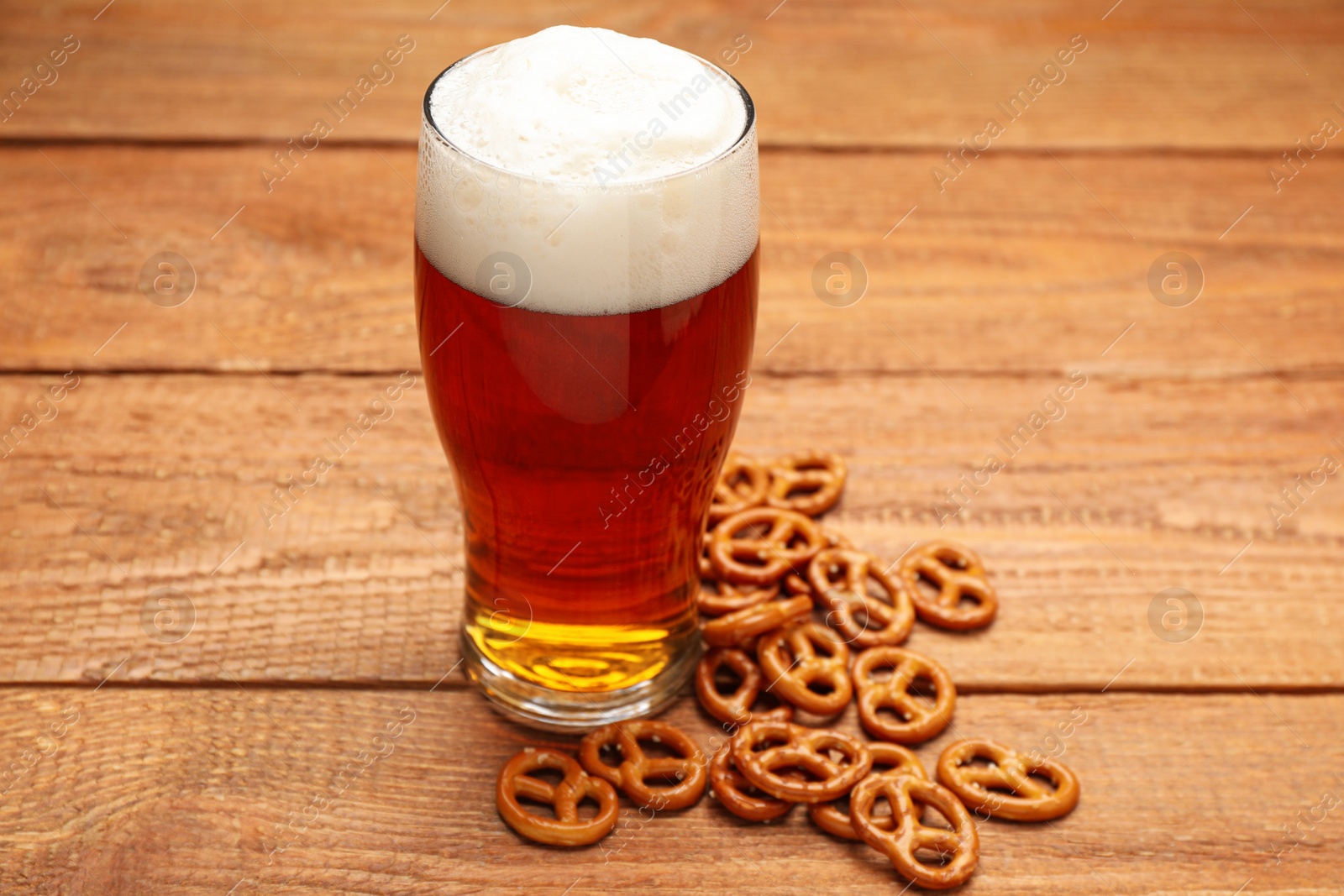 Photo of Delicious pretzel crackers and glass of beer on wooden table