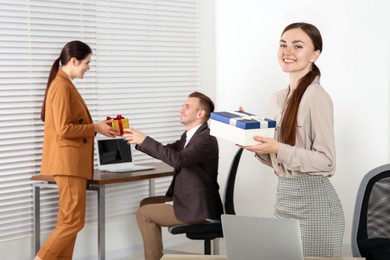 Photo of Happy woman holding gift box and man taking present from his colleague in office