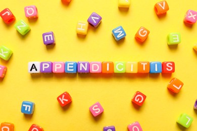 Photo of Word Appendicitis made of color cubes with letters on yellow background, flat lay