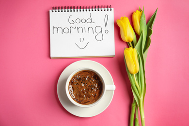 Delicious coffee, beautiful flowers and GOOD MORNING wish on pink background, flat lay