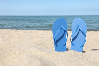 Stylish blue flip flops on beach sand, space for text