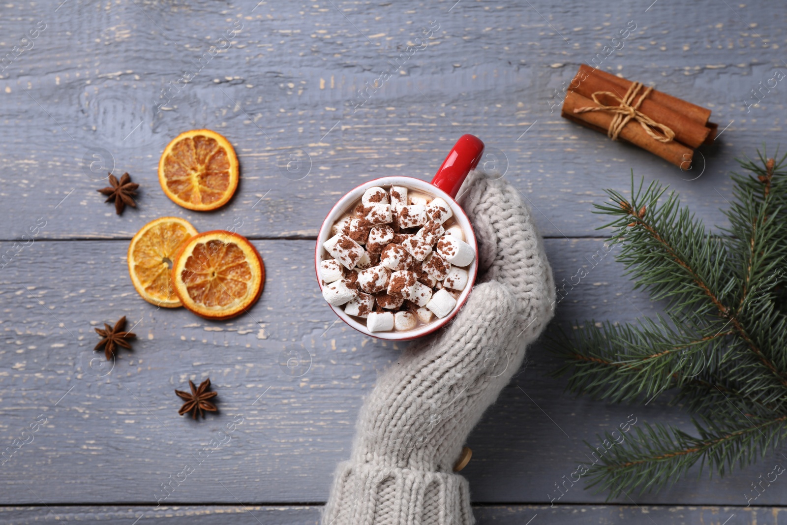 Photo of Person holding cup of tasty cocoa with marshmallows on grey wooden table, top view