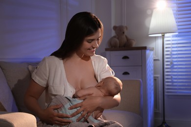 Young woman breastfeeding her little baby indoors at night