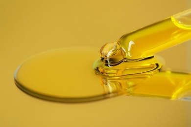 Photo of Dripping face serum from pipette on yellow background, closeup