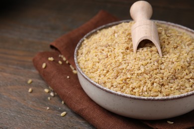 Photo of Bowl and scoop with raw bulgur on wooden table, closeup. Space for text