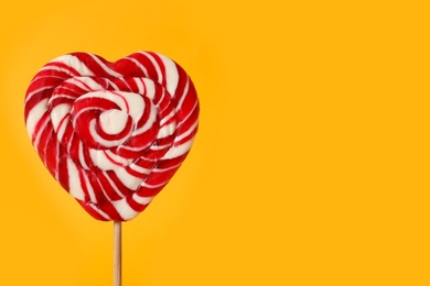 Photo of Sweet heart shaped lollipop on orange background, closeup view with space for text. Valentine's day celebration