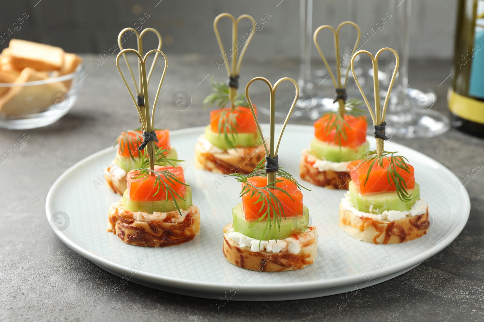 Photo of Tasty canapes with salmon, cucumber, bread and cream cheese on grey table