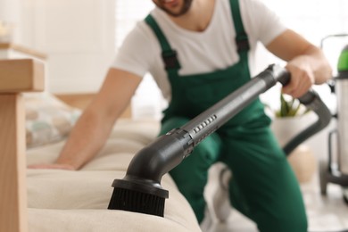 Photo of Professional janitor vacuuming sofa in living room, focus on nozzle