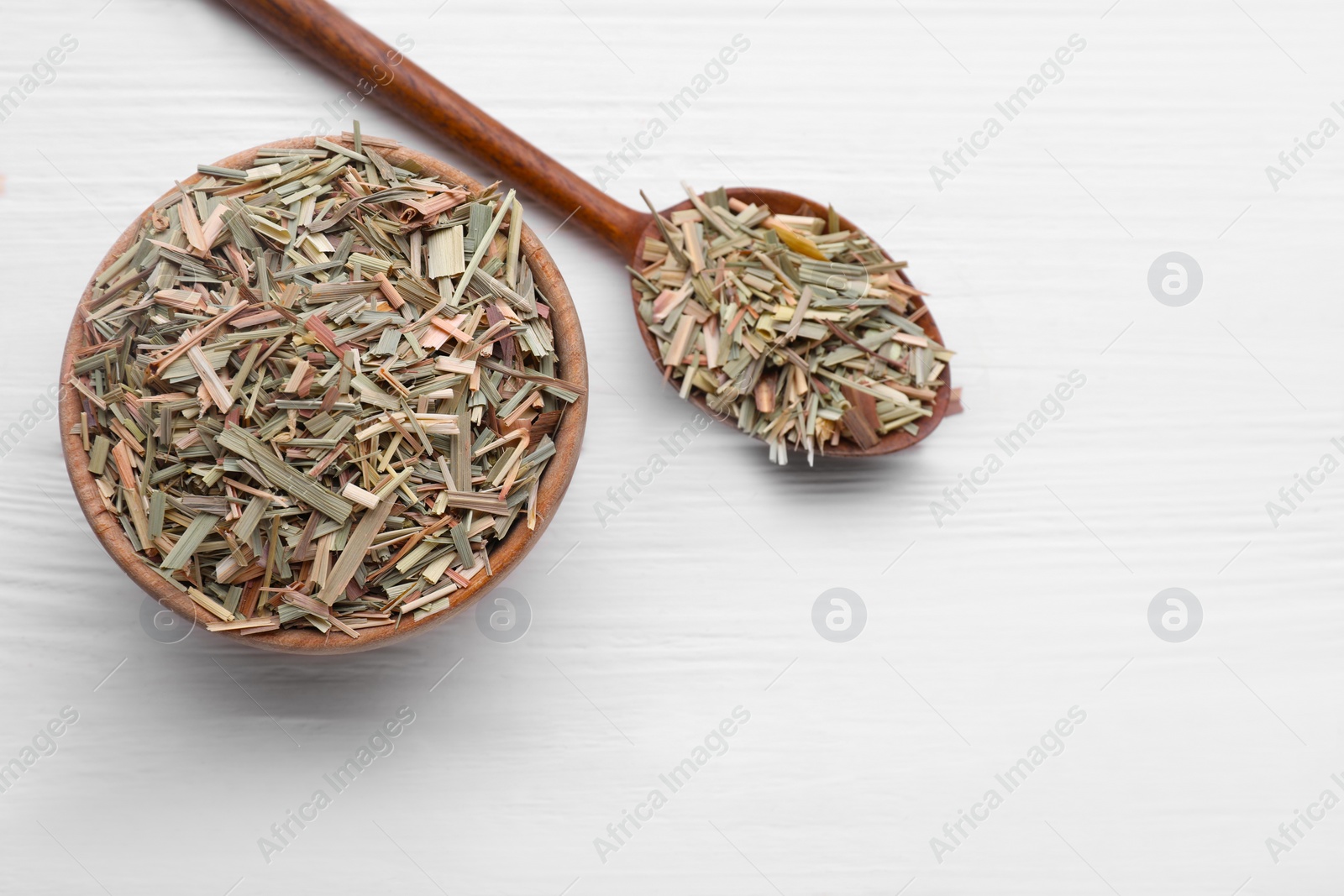 Photo of Bowl and spoon with aromatic dried lemongrass on white wooden table, flat lay. Space for text