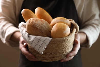 Photo of Man holding wicker basket with different types of bread on brown background, closeup