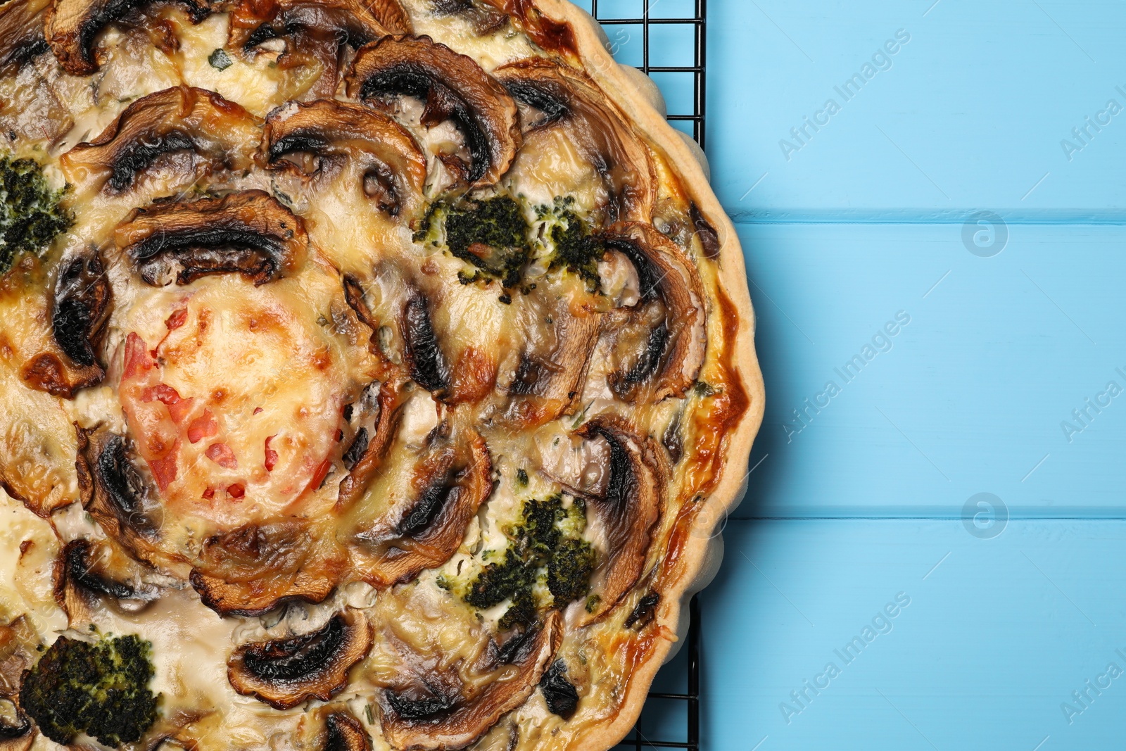 Photo of Delicious quiche with mushrooms on light blue wooden table, top view. Space for text
