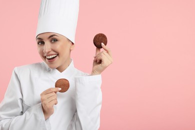 Photo of Happy professional confectioner in uniform holding delicious macarons on pink background. Space for text