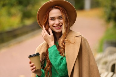 Smiling woman with paper cup in autumn park