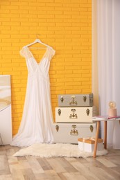 Photo of Stylish room interior with storage trunks and beautiful wedding dress near yellow brick wall
