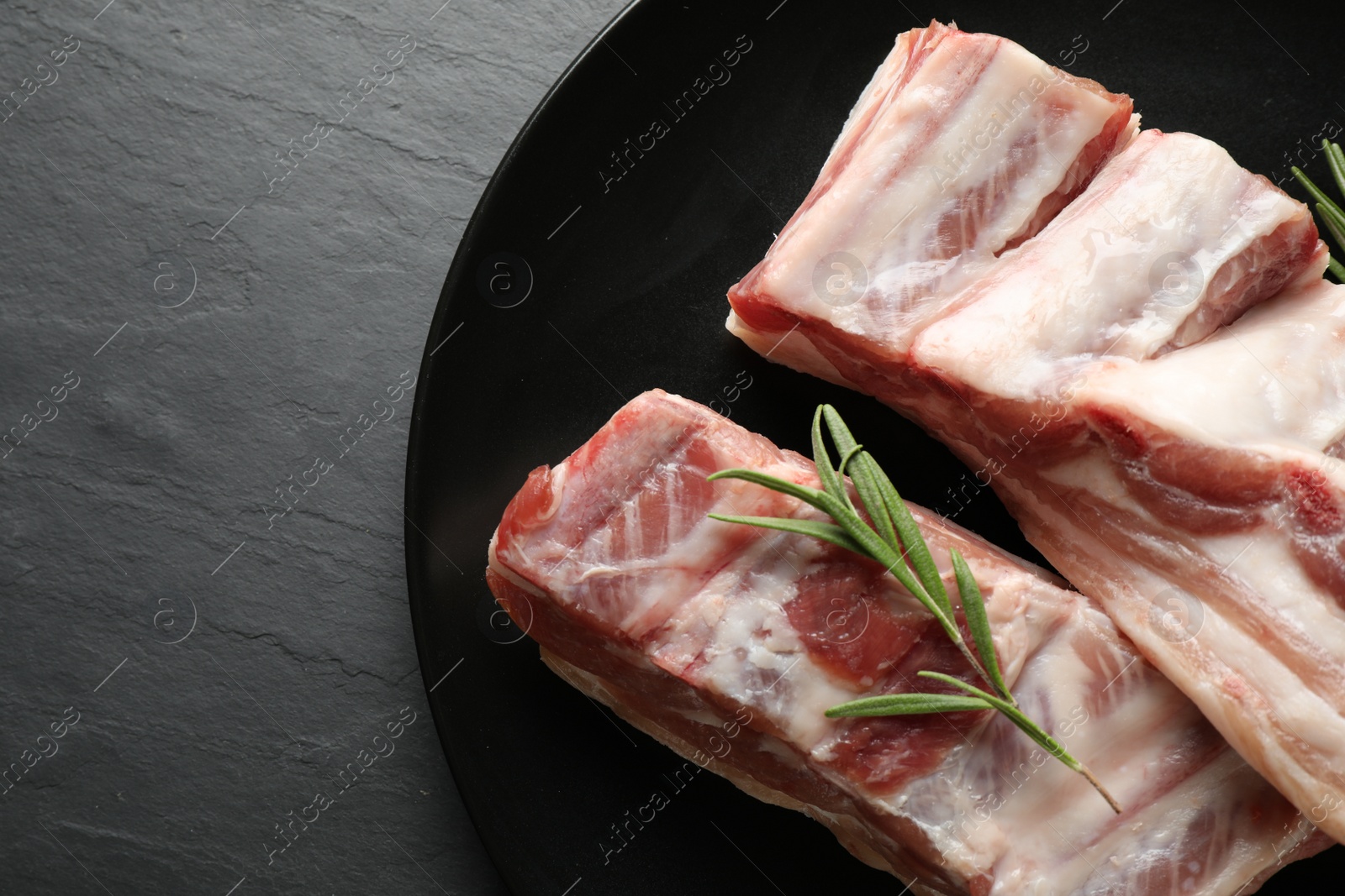 Photo of Raw ribs with rosemary on black table, top view