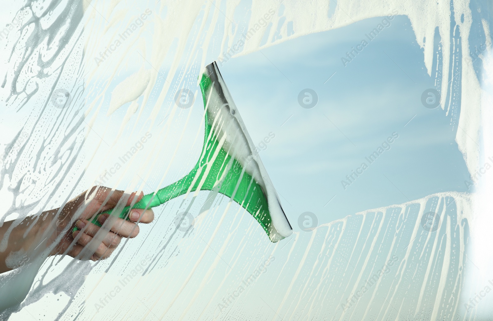 Photo of Woman cleaning window with squeegee on spring day, closeup