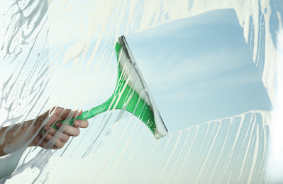 Photo of Woman cleaning window with squeegee on spring day, closeup