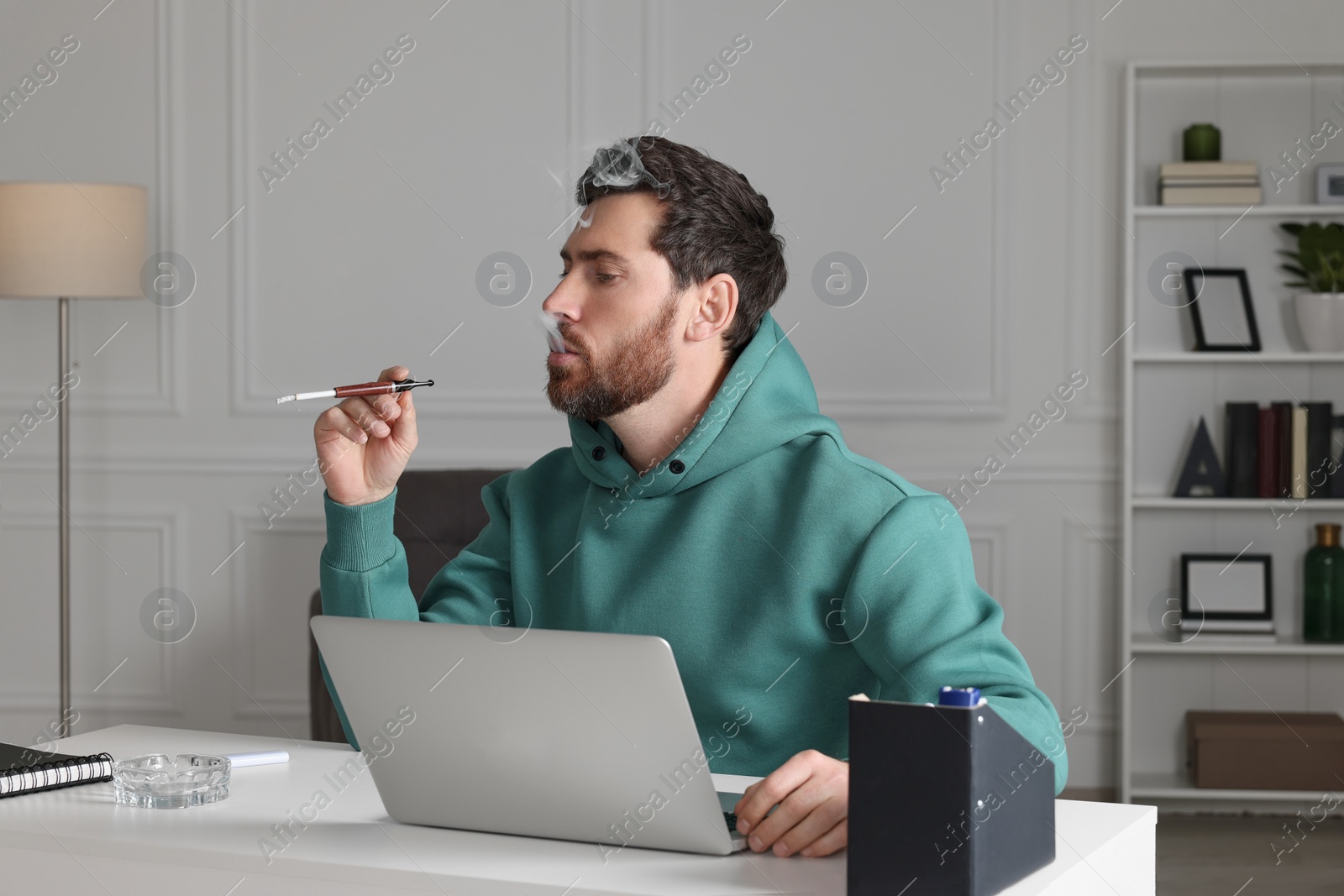 Photo of Man using cigarette holder for smoking at workplace in office