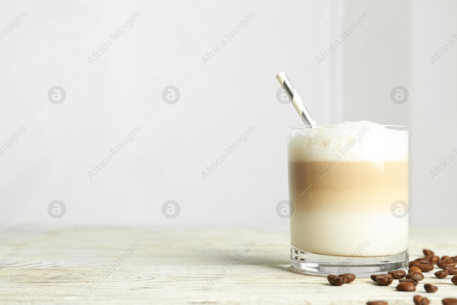 Photo of Delicious latte macchiato and coffee beans on white wooden table indoors, space for text