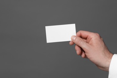 Photo of Man holding blank business card on grey background, closeup. Space for text