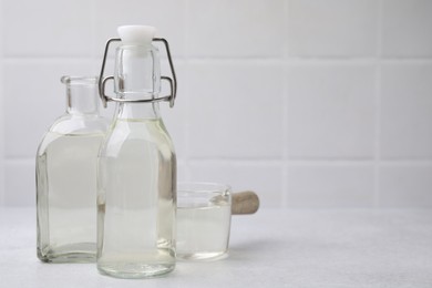 Photo of Vinegar in glass bottles and saucepan on light table, space for text