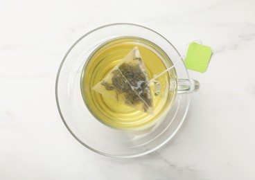 Tea bag in glass cup on white table, top view
