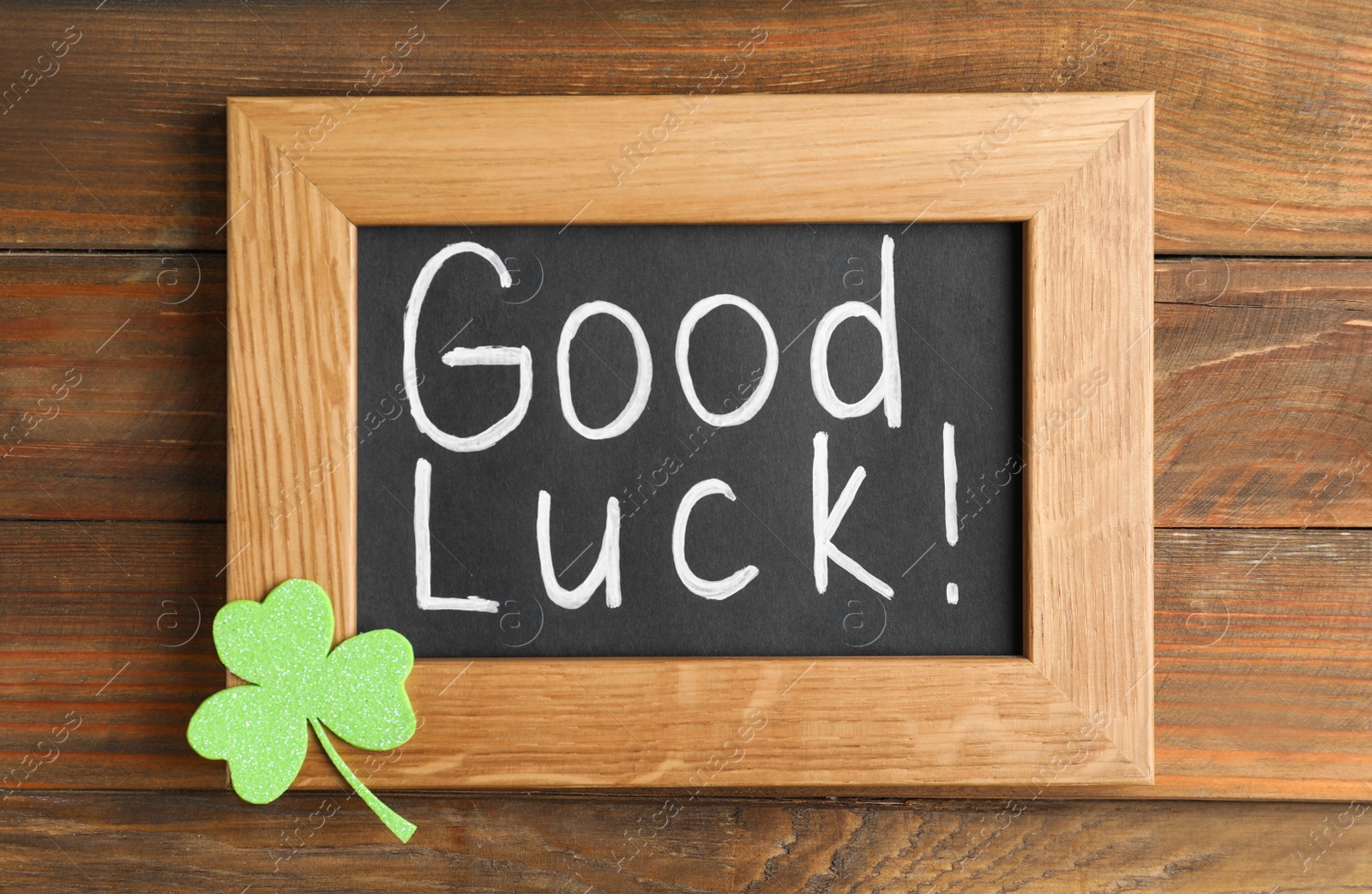 Photo of Blackboard with phrase GOOD LUCK and clover leaf on wooden table, top view