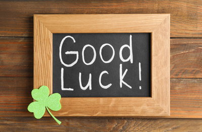 Blackboard with phrase GOOD LUCK and clover leaf on wooden table, top view