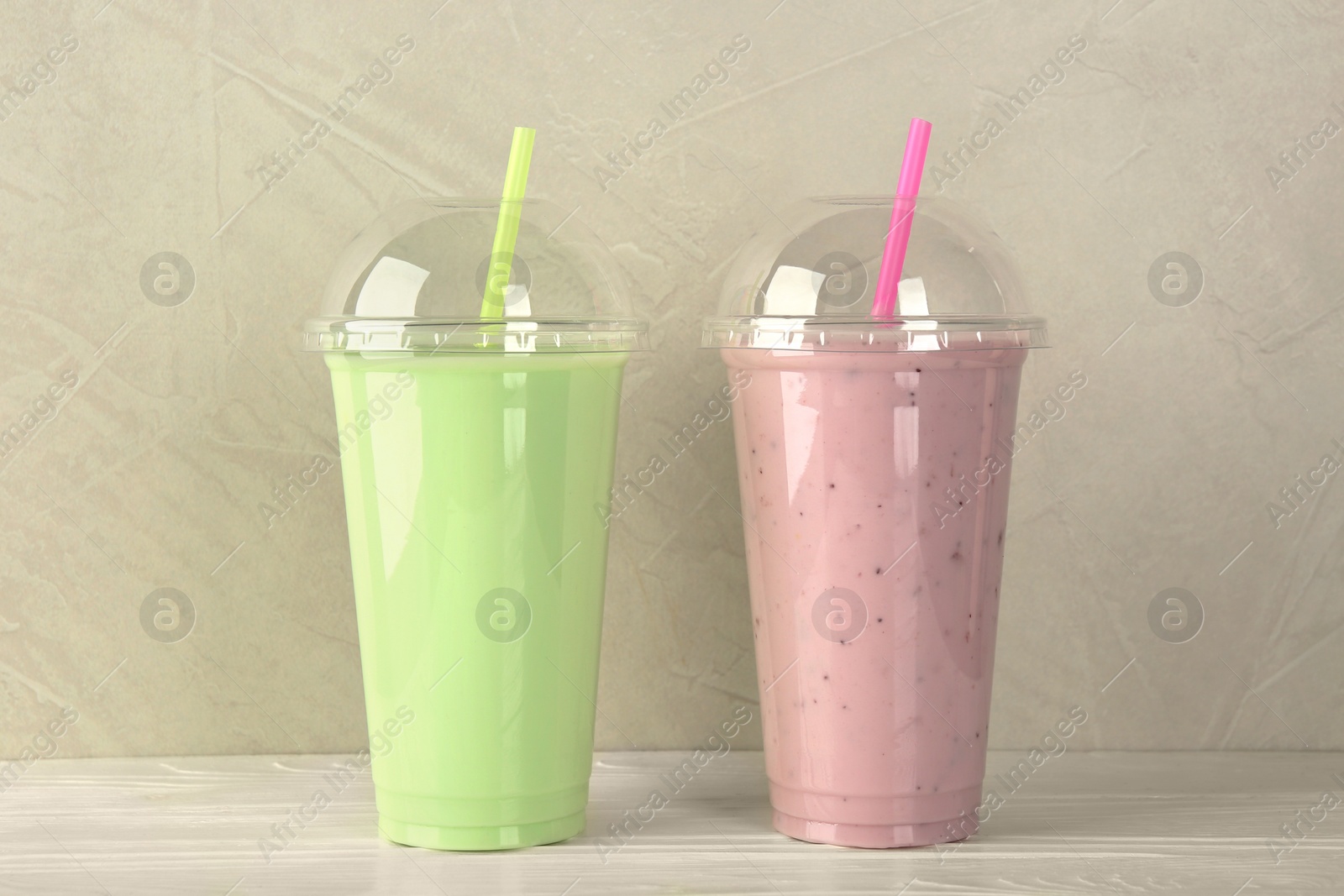 Photo of Plastic cups of different tasty smoothie on white wooden table