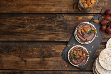 Photo of Puffed rice cakes with chocolate spread, nuts and mint on wooden table, flat lay. Space for text