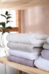 Photo of Stacked soft towels and green leaves on wooden shelf indoors