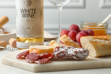 Photo of Delicious sausage, bread and bottle of white wine on table, closeup