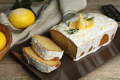 Tasty lemon cake with glaze and citrus fruits on wooden table, closeup