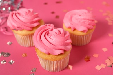 Photo of Delicious cupcakes with bright cream and confetti on pink table, closeup