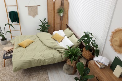 Photo of Stylish bedroom with comfortable bed and beautiful green houseplants, above view. Interior design