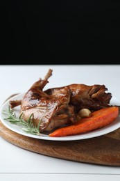 Tasty cooked rabbit meat with rosemary, garlic and carrot on white wooden table. Space for text