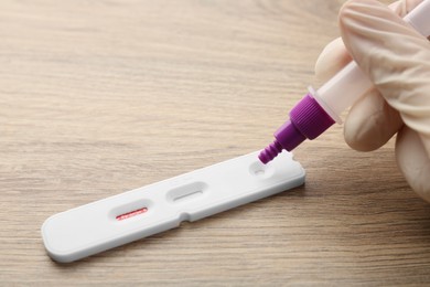 Doctor dropping buffer solution onto Covid-19 express test cassette at wooden table, closeup