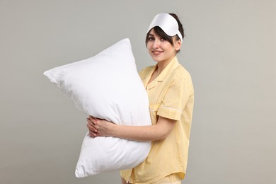 Photo of Happy woman in pyjama and sleep mask holding pillow on grey background