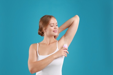 Photo of Young woman applying deodorant to armpit on teal background