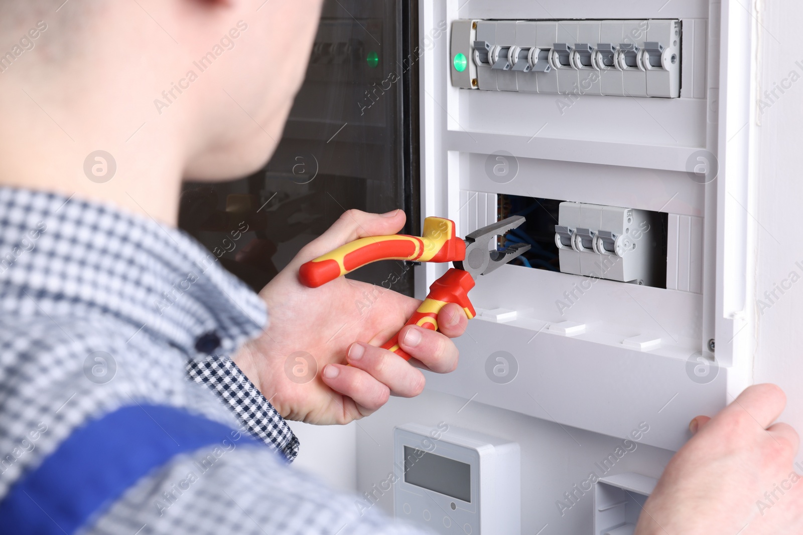 Photo of Professional repairman fixing electric panel with pliers indoors, closeup