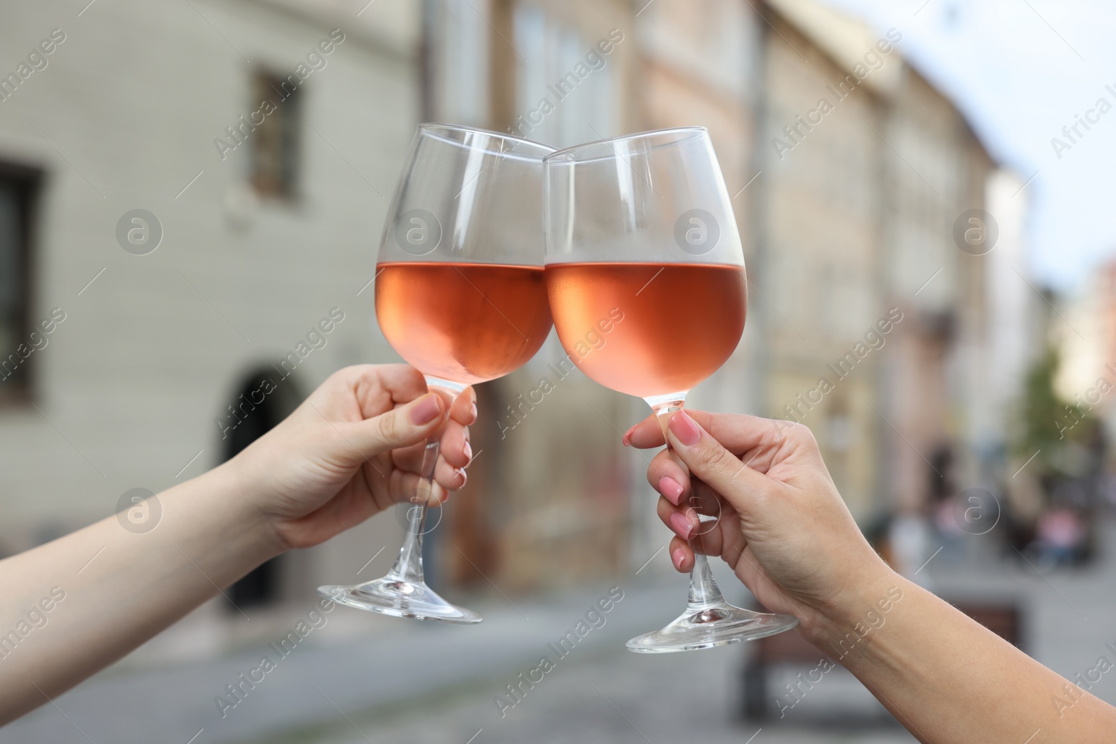 Photo of Women clinking glasses with rose wine outdoors, closeup