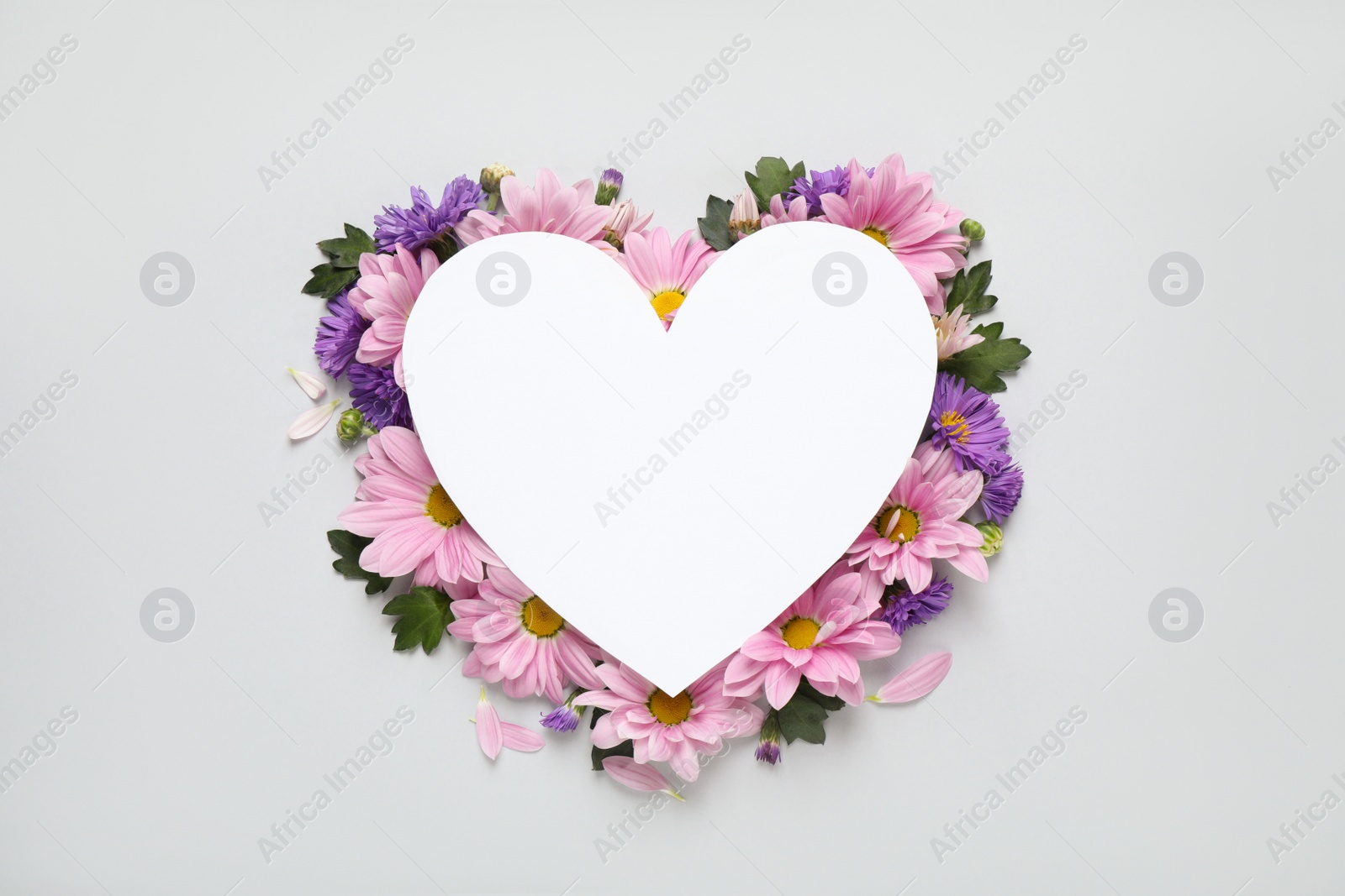 Photo of Beautiful chamomile flowers and heart shaped paper card on white background, top view with space for text